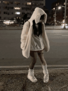 a girl wearing a white hoodie with bunny ears is standing on a sidewalk