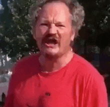 a man with a mustache and a red shirt is making a funny face .