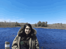 a woman in a green jacket stands in front of a body of water