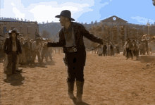 a man in a cowboy hat is standing in a dirt field in front of a building that says ' the city '