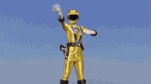 a yellow power ranger is wearing a yellow helmet and gloves and is standing in the rain .
