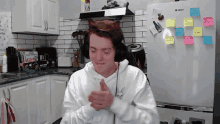 a man wearing headphones is giving a thumbs up in front of a refrigerator that has sticky notes on it