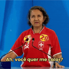 a woman in a red shirt is standing in front of two microphones and talking into them .