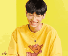 a man wearing glasses and a yellow shirt that says hug on it