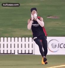 a man is running on a field with a fence in the background and a sign that says icc .