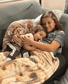 two children are sitting on a couch with a blanket that looks like a pizza .