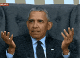 a man in a suit and tie is sitting in a chair with his hands outstretched in front of a sign that says siburg