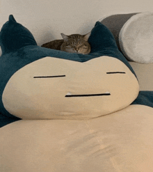 a cat laying on top of a stuffed animal that looks like a snorlax