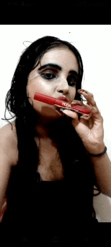 a woman with black makeup is holding a red mascara in her mouth .