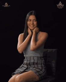 a woman in a gray top and plaid skirt is sitting in front of a black background that says miss universe thailand