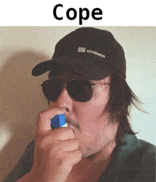 a man wearing sunglasses and a hat is blowing a blue cube into his mouth .