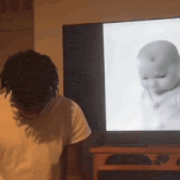 a man is standing in front of a television with a baby on the screen
