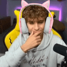 a young man wearing pink cat ears headphones is sitting in a yellow chair .