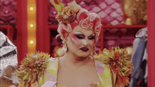 a drag queen is wearing a colorful costume with flowers and feathers on her shoulder .