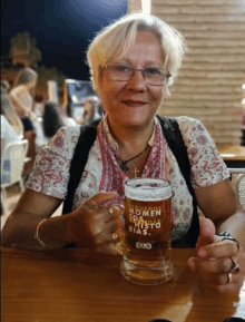 a woman sits at a table holding a mug of beer that says " mujeres somen a cristo dias "