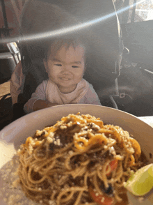 a baby sits in a stroller looking at a plate of spaghetti