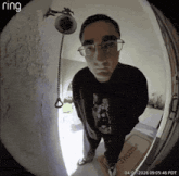 a man wearing glasses is standing in front of a door with a welcome mat on it .