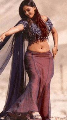 a woman in a purple crop top and purple skirt is standing on a beach .