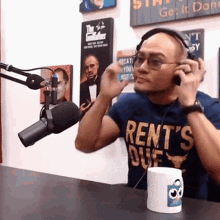 a man wearing headphones and a rent 's due shirt talks into a microphone