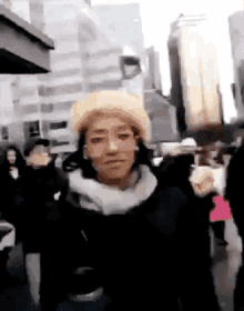 a woman wearing a hat and scarf is walking down a street in a crowd of people .