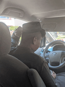 a man wearing a hat driving a toyota