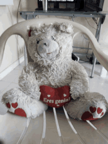 a teddy bear sits in a chair holding a heart that says " eres genial "