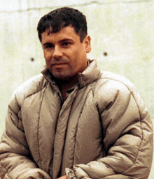 a man wearing a puffy jacket stands in front of a wall