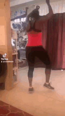 a woman in a red tank top and black leggings is dancing in a living room .