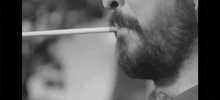 a close up of a man with a beard smoking a cigarette in a black and white photo .