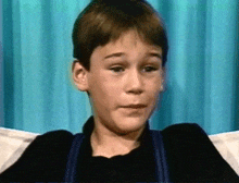 a young boy is sitting in front of a blue curtain looking at the camera