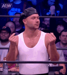 a man wearing a white tank top and a black hat is standing in front of a crowd that is watching a wrestling show