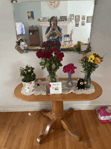 a woman is taking a picture of herself in front of a mirror with flowers on the table