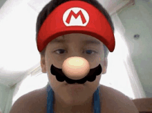 a young boy wearing a mario hat and mustache is looking at the camera .