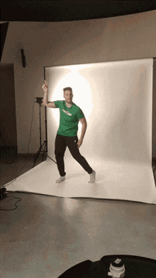 a man in a green shirt that says ' t-shirt ' on it stands in front of a white backdrop