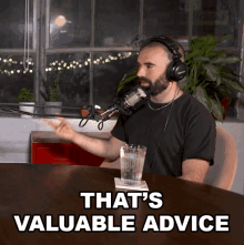 a man wearing headphones sits at a table with a glass of water and the words that 's valuable advice above him