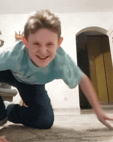 a young boy in a blue shirt is smiling while crawling on the floor