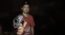 a man in a red shirt is pointing a gun at the camera in a dark room .