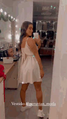 a woman in a white dress is taking a picture of herself in the mirror