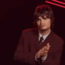 a man in a suit and tie is clapping his hands on a stage .