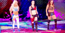 three female wrestlers are standing on a stage and one of them is wearing a blue shirt