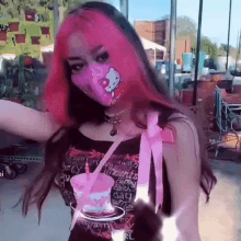 a girl with pink hair and a hello kitty mask is holding a pink cup .