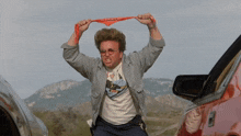 a man wearing a bandana that says ' no smoking ' on it is standing in front of a red car