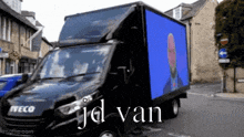 a black iveco van with a blue screen on the back is parked on the street .