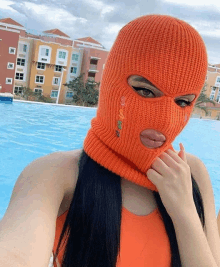 a woman wearing an orange ski mask takes a selfie by a pool