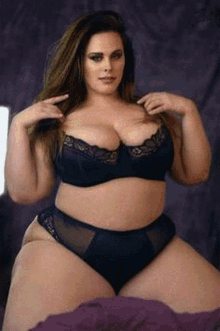 a plus size model is sitting on a bed wearing black lingerie .