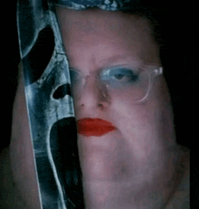 a woman with glasses and red lips is holding a knife