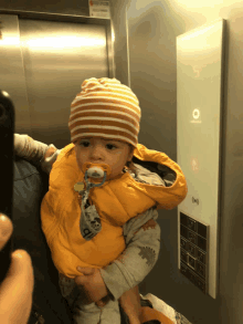 a baby with a pacifier in his mouth is in an elevator with the number 5 on the wall