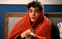 a man with curly hair is wrapped in an orange knitted blanket