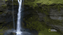 a man is hanging from a rope in front of a waterfall with the national geographic logo on the bottom right