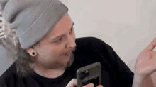 a man wearing a gray beanie and a black shirt is looking at his phone